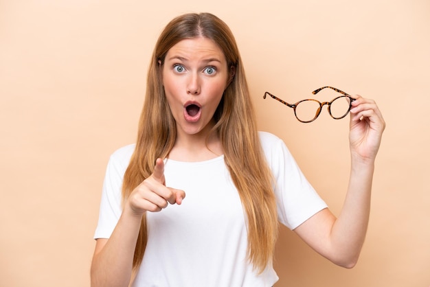 Young pretty blonde woman with glasses isolated on beige background surprised and pointing front