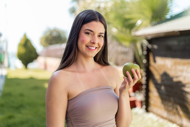 Young pretty Brazilian woman at outdoors with an apple