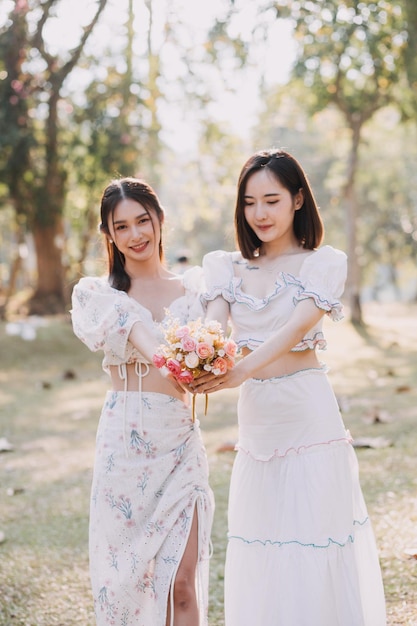 Young pretty brunette twin girls sitting on the grass with legs slightly bent in knees and looking in a brown book wearing casual coat in autumn sunny weather on blurry background