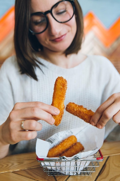 Young pretty brunette woman eats fried cheese sticks from a decorated iron basket in a cafe. Fast food. Toning.