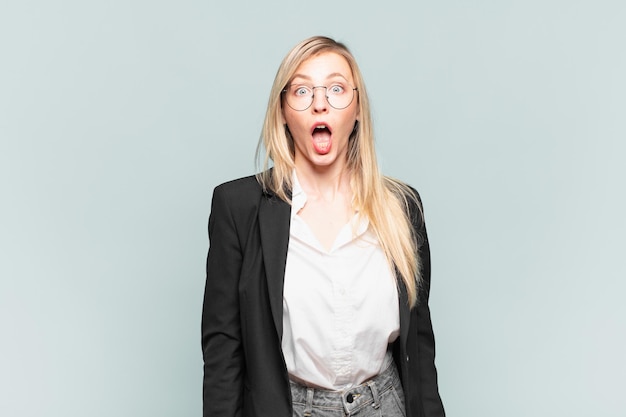 Young pretty businesswoman feeling terrified and shocked, with mouth wide open in surprise