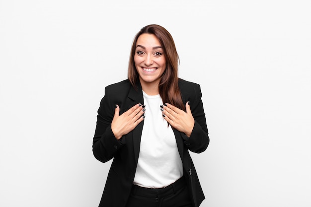 Young pretty businesswoman looking happy, surprised, proud and excited, pointing to self against white wall