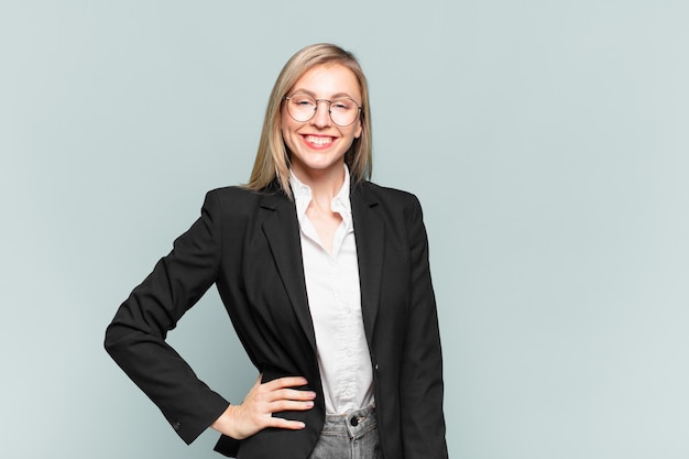 Young pretty businesswoman smiling happily with a hand on hip and confident, positive, proud and friendly attitude