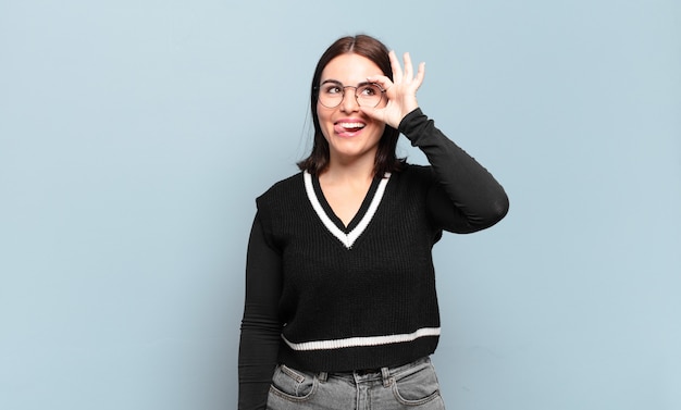 Young pretty casual woman smiling happily with funny face, joking and looking through peephole, spying on secrets