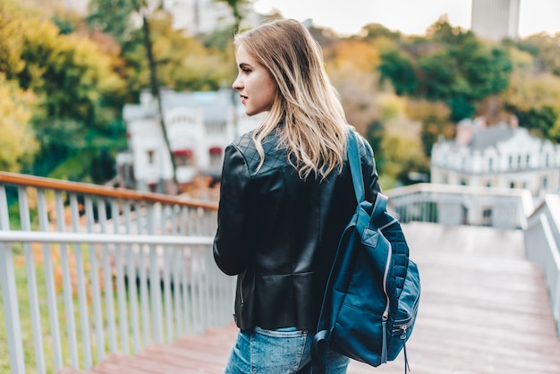 Young pretty casually dressed hipster girl tourist posing outdoors at the city park steps with a backpack