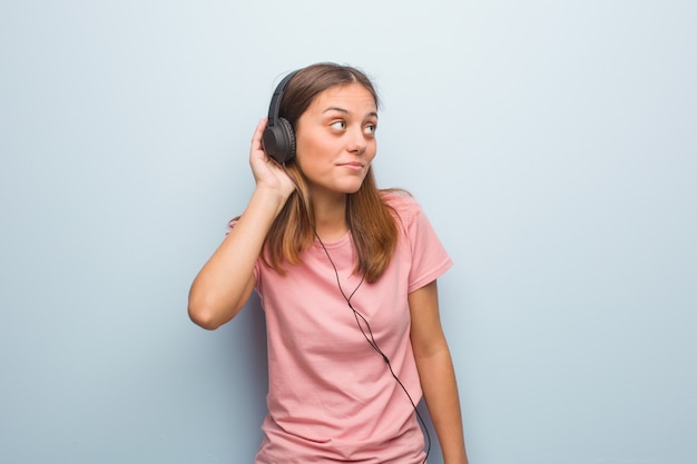 Young pretty caucasian woman try to listening a gossip. She is listening to music with headphones.