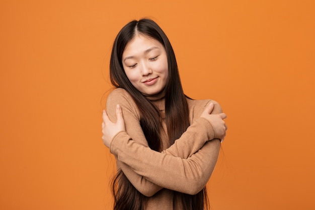 Young pretty chinese woman hugs himself, smiling carefree and happy.