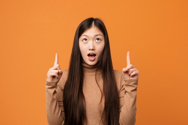 Young pretty chinese woman pointing upside with opened mouth.