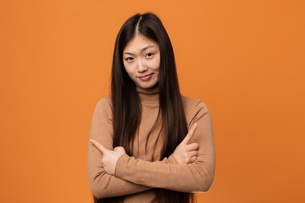 Young pretty chinese woman points sideways, is trying to choose between two options.