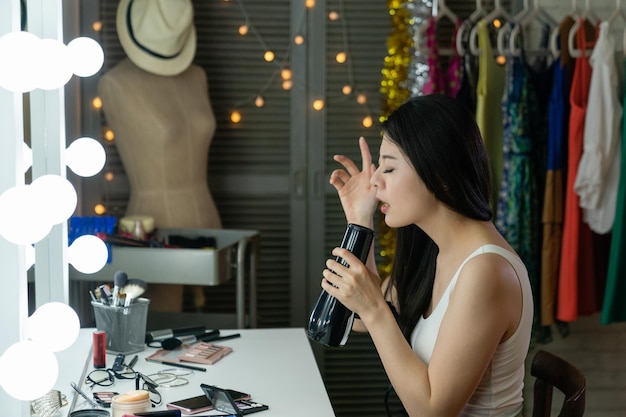 Young pretty chinese woman singer singing with hair dryer instead microphone in dressing room sitting at vanity table. nervous asian girl practicing for show enjoy songs melody music in backstage.