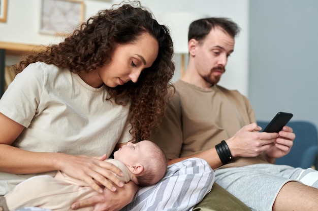 Young pretty female looking at sleeping baby on her hands in the morning