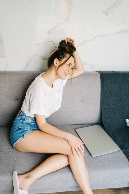 young pretty female online shopping on laptop she is laying on couch typing on laptop