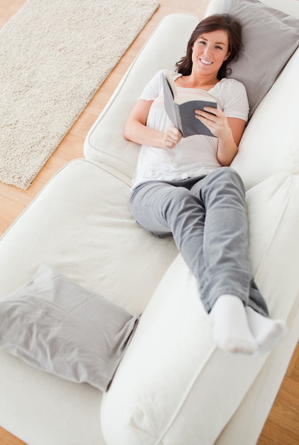 Young pretty female reading a book while lying on a sofa