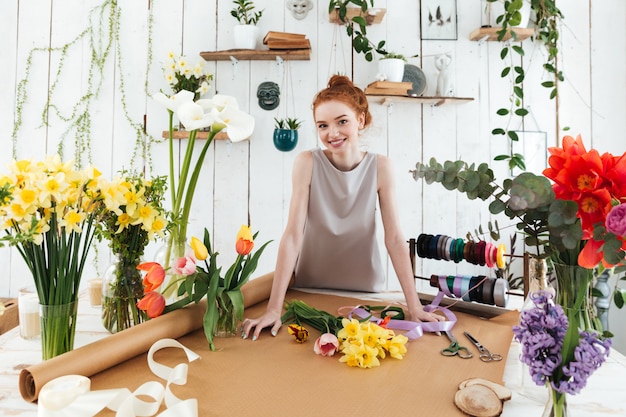 Young pretty florist standing near table with flowers