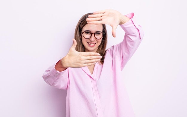 Young pretty girl feeling happy, friendly and positive, smiling and making a portrait or photo frame with hands