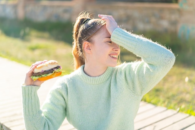 Young pretty girl holding a burger at outdoors has realized something and intending the solution