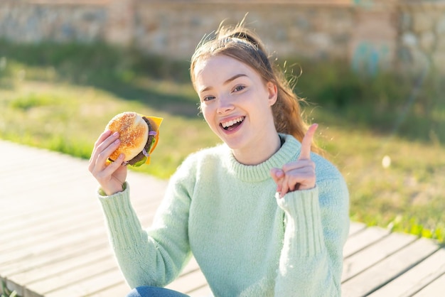 Young pretty girl holding a burger at outdoors pointing up a great idea