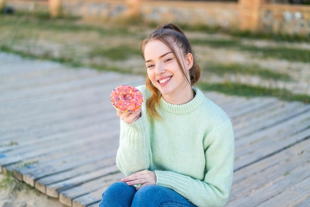 Young pretty girl holding a donut at outdoors with happy expression