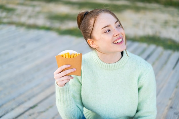 Young pretty girl holding fried chips at outdoors looking up while smiling