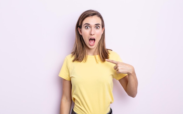 Young pretty girl looking shocked and surprised with mouth wide open, pointing to self