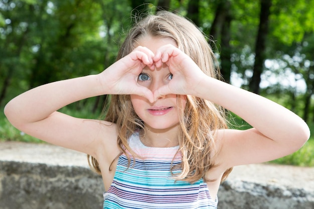 Photo a young pretty girl makes a heart with her hands in front of her face