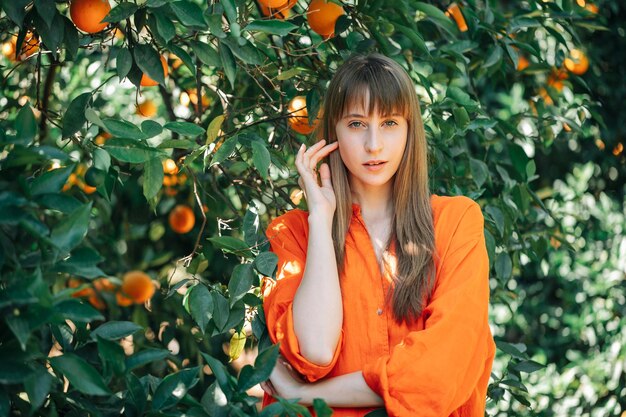 Young pretty girl in orange dress posing to camera in orange garden