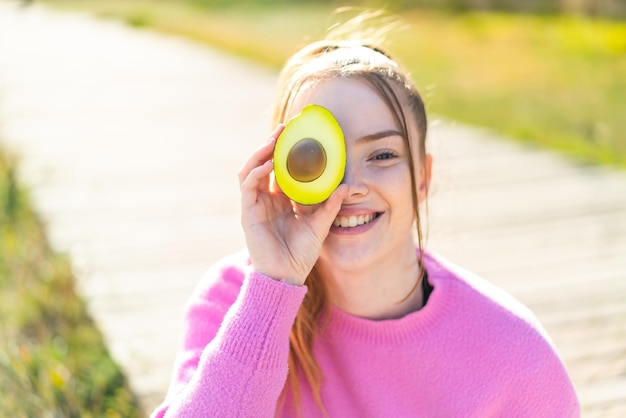 Young pretty girl at outdoors holding an avocado with happy expression