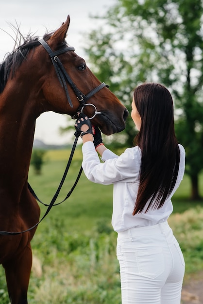 A young pretty girl rider poses near a thoroughbred stallion on a ranch