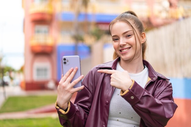 Young pretty girl using mobile phone at outdoors and pointing it