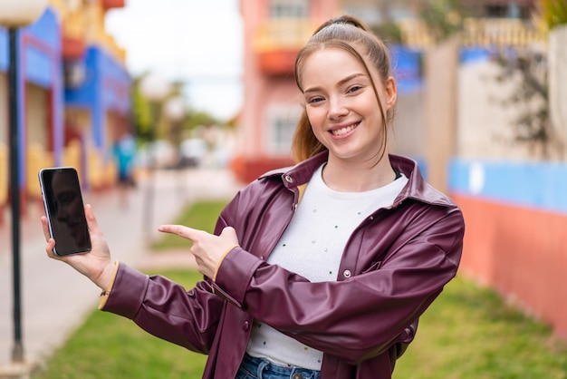 Young pretty girl using mobile phone at outdoors and pointing it