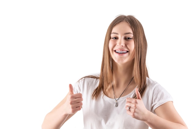 Young pretty girl with braces is showing thumbs up isolated on white