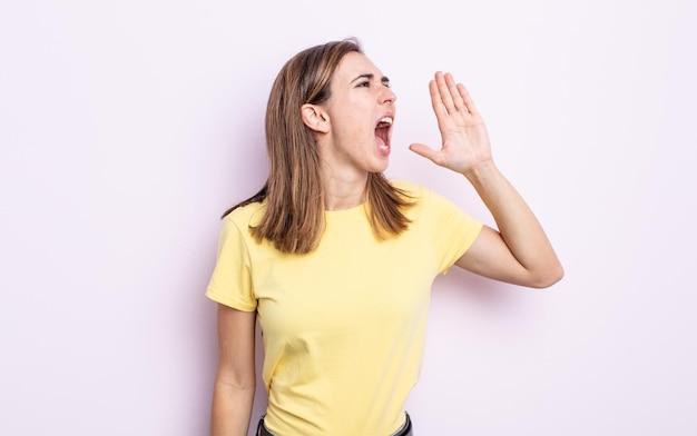 Young pretty girl yelling loudly and angrily to copy space on the side, with hand next to mouth