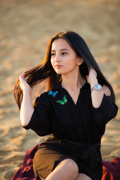 Young pretty hispanic gir in black sit on sand