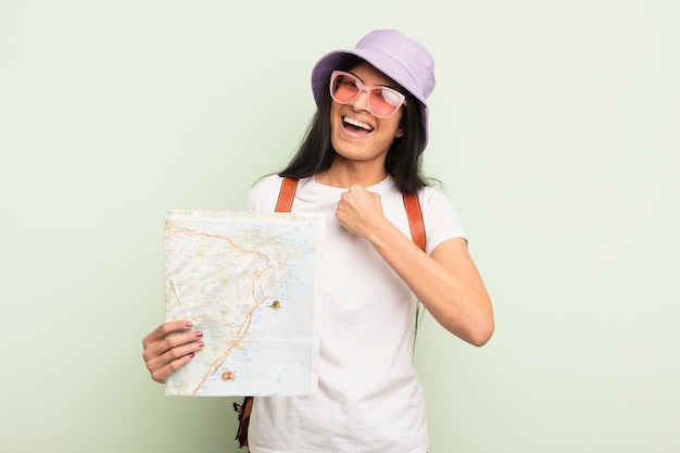 Young pretty hispanic woman feeling happy and facing a challenge or celebrating tourist and map concept