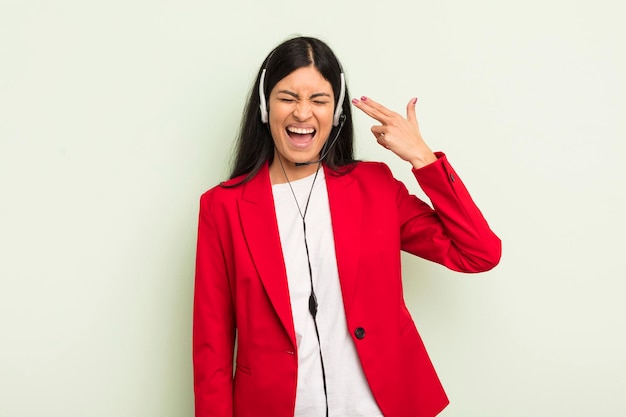 Young pretty hispanic woman looking unhappy and stressed suicide gesture making gun sign telemarteker concpet