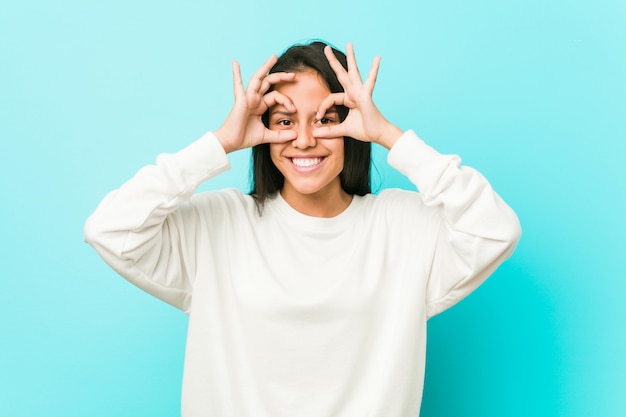 Young pretty hispanic woman showing okay sign over eyes