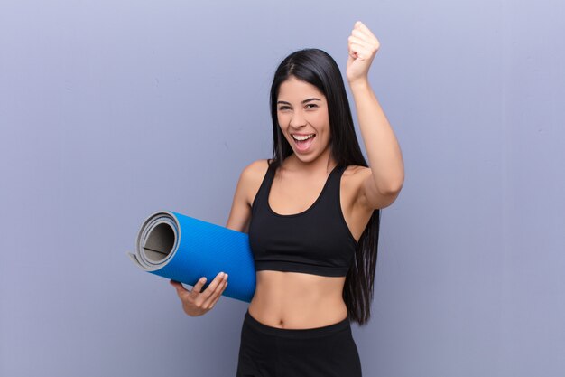 Young pretty lating woman with a yoga mat against cement wall