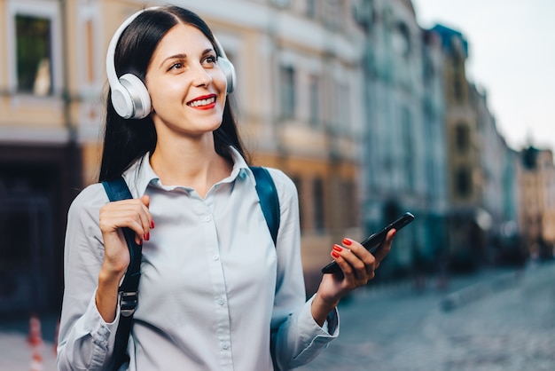 Young pretty long haired tourist woman with a backpack enjoying the walk through the old city street and listening to music