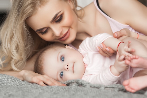 Young pretty mother with her little baby at home. Mom and daughter indoors.  month child with her parent in the bedroom.