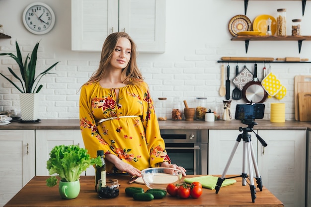 Photo young pretty pregnant girl blogger shoots a video of a salad recipe on a smartphone camera