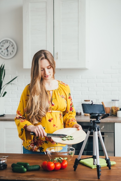 Young pretty pregnant girl blogger shoots a video of a salad recipe on a smartphone camera