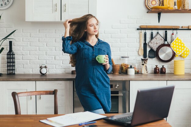 Young pretty pregnant girl works at home in self-isolation mode in quarantine and takes a break for rest with coffee