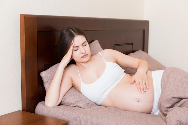 Young pretty pregnant woman suffering from headache at home in bed