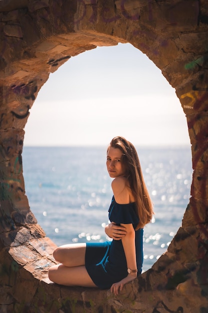 A young pretty redhaired Caucasian woman sitting in a blue dress by the sea