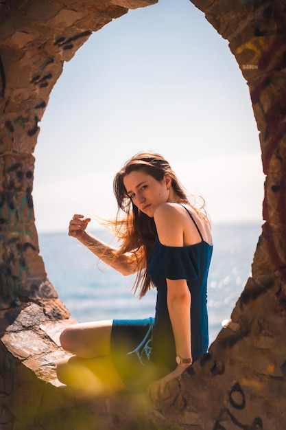 A young pretty redhaired Caucasian woman sitting in a blue dress by the sea