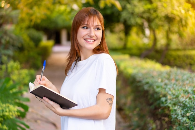 Young pretty redhead woman at outdoors holding a notebook