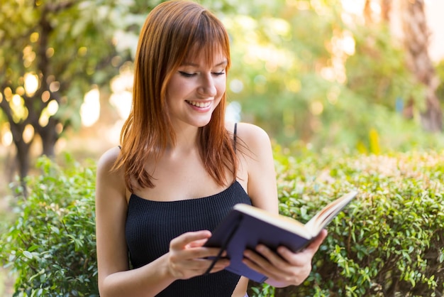 Young pretty redhead woman at outdoors holding a notebook