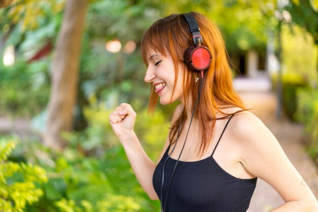 Young pretty redhead woman at outdoors listening music and dancing