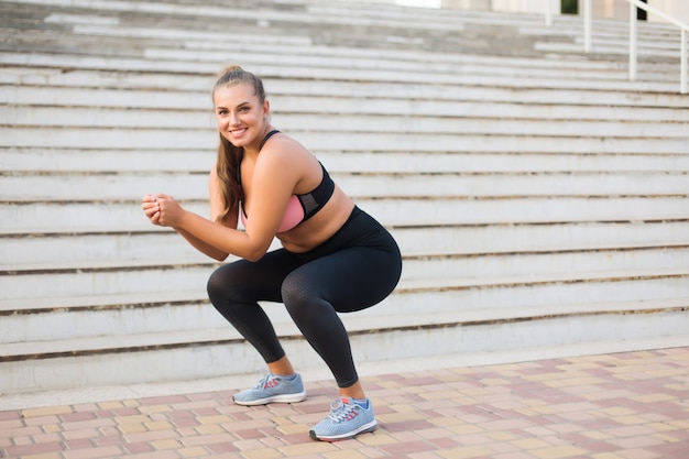 Young pretty smiling plus size woman in sporty top and leggings doing sport with stairs 