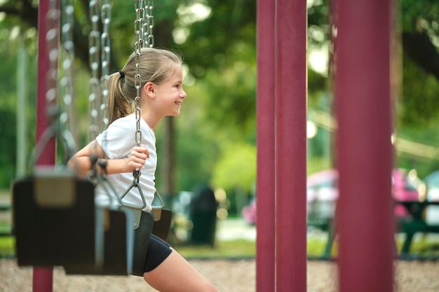 Young pretty smiling teenage girl playing alone on swings on summer playground